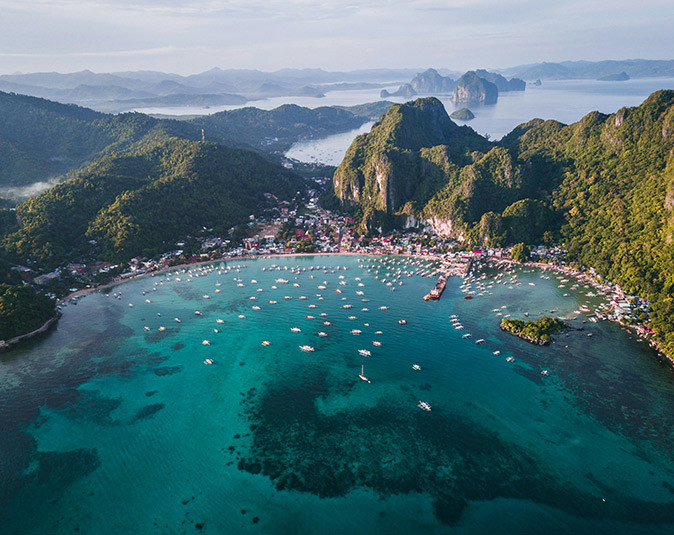 Snorkeling in El Nido, Palawan Aerial view of a tropical island showing green mountains, sandy beaches, bright blue water and a lot of small boats in a bay