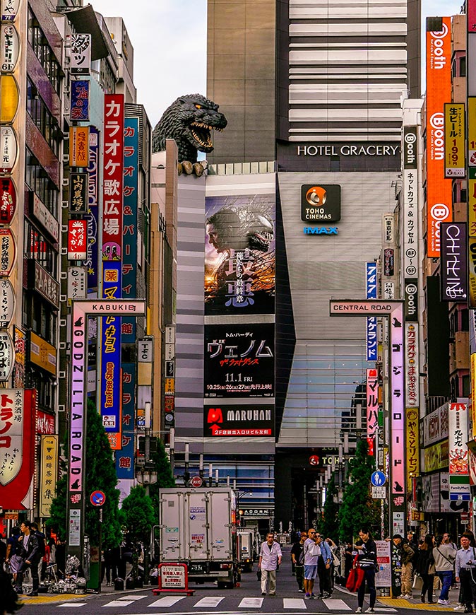 Nerdy things to do in Tokyo A typical street in Tokyo with highrise buildings filled with signs, and a Godzilla head showing above one of the buildings
