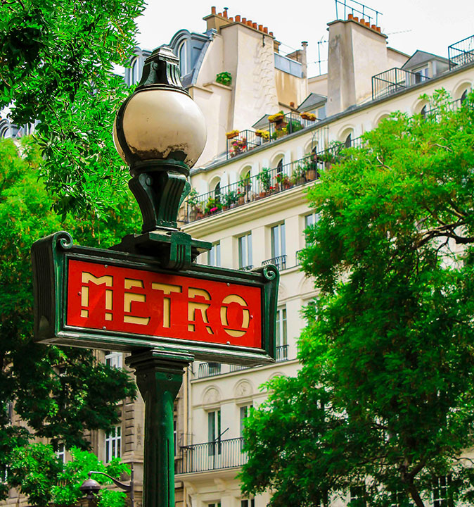 Getting around in Paris A red and yellow metro sign on a lamp post with a beige building and trees in the background