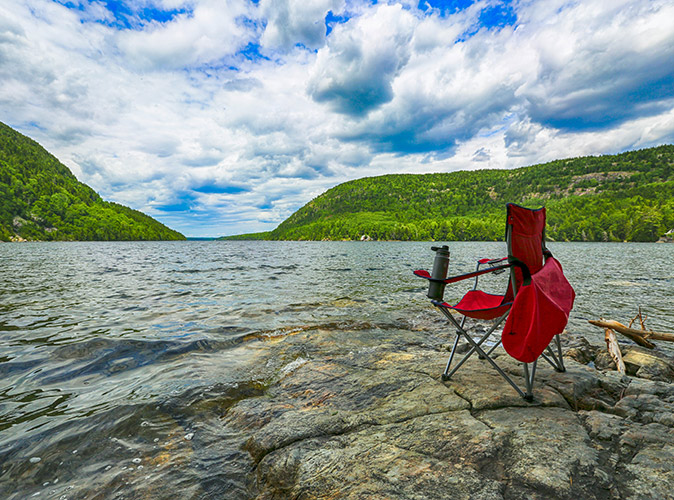 The best time for RVing in Maine A red folding chair on the side of a lake with green hills in the background