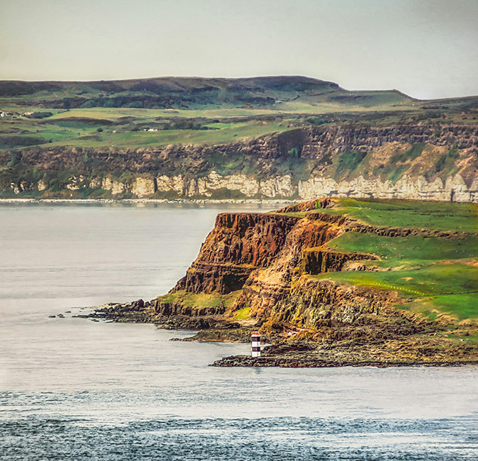 A place I'd recommend visiting in Northern Ireland A ruggid coastline showing high cliffs and green land under a moody sky