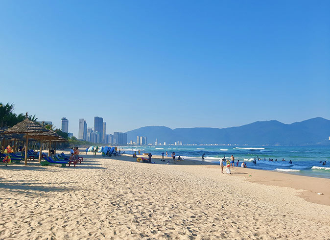 My Khe Beach, part of a Da Nang 2 day itinerary A white sandy beach with a few umbrellas and high rise in the background