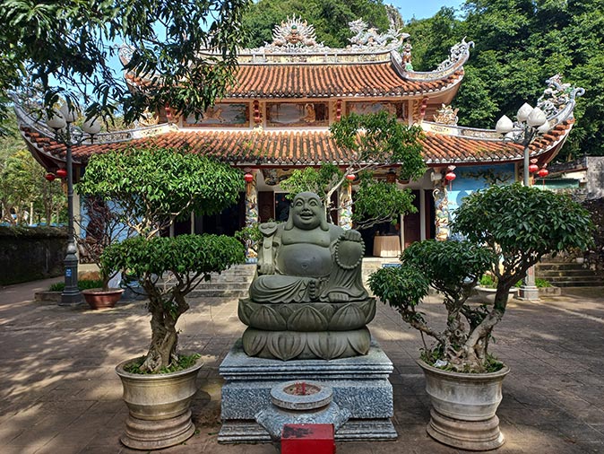a temple with a double red roof and a large buddha statue in front of it, surrounded by trees