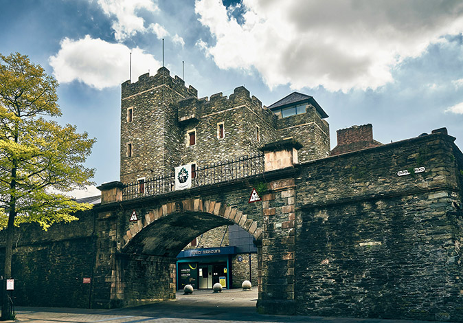 One of the best places to visit in Northern Ireland A gray, old city wall with a gate and a castle looking structure behind it