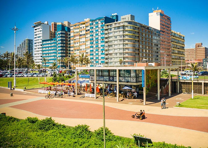 A restaurant on a paved boardwalk with high rise buildings in the background