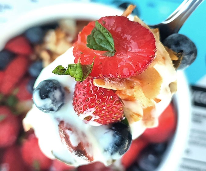 close-up of a spoon with fruit and yoghurt above a breakfast bowl