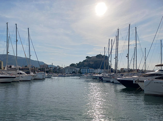 A marina with several boats looking towards a typical Spanish town with a castle on the hill in the background