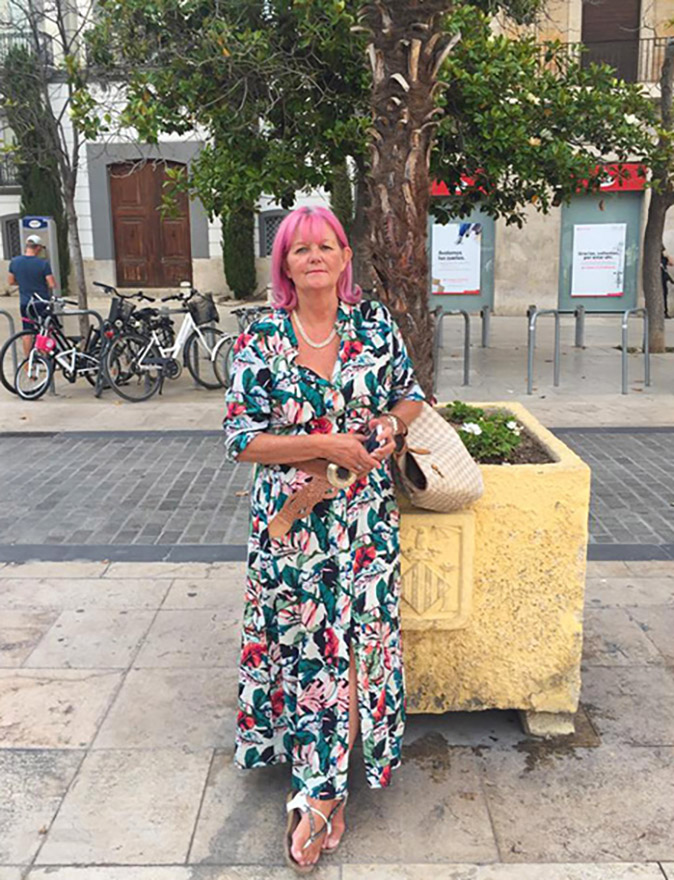 A woman with pink hair staninding in front of a tree in a Spanish city