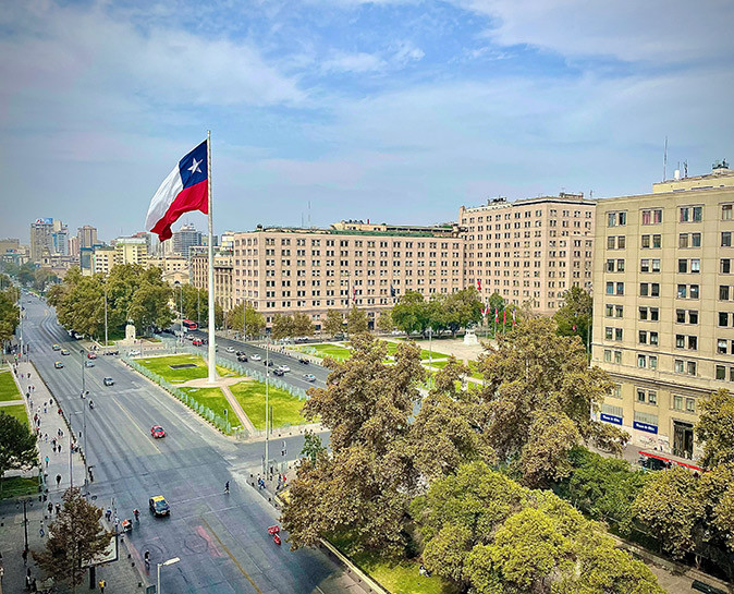 Life in Santiago, Chile A city with a wide road, some greenery, large apartment buildings and a large flag of Chile