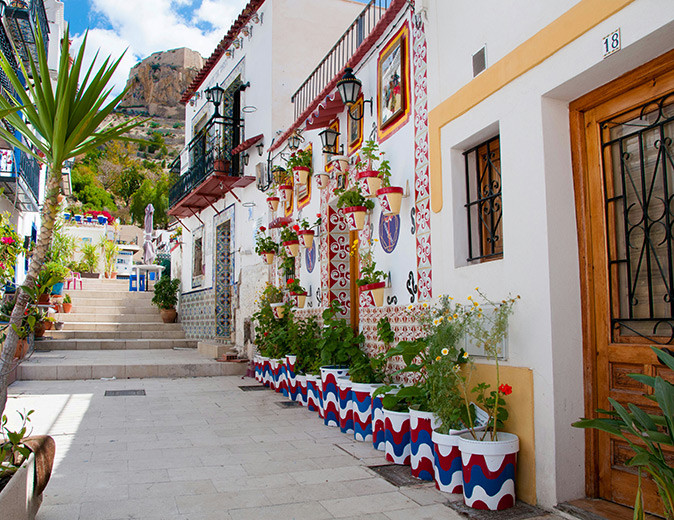 A narrow street with whitewashed, typical Spanish houses with a lot of potted plants and some trees