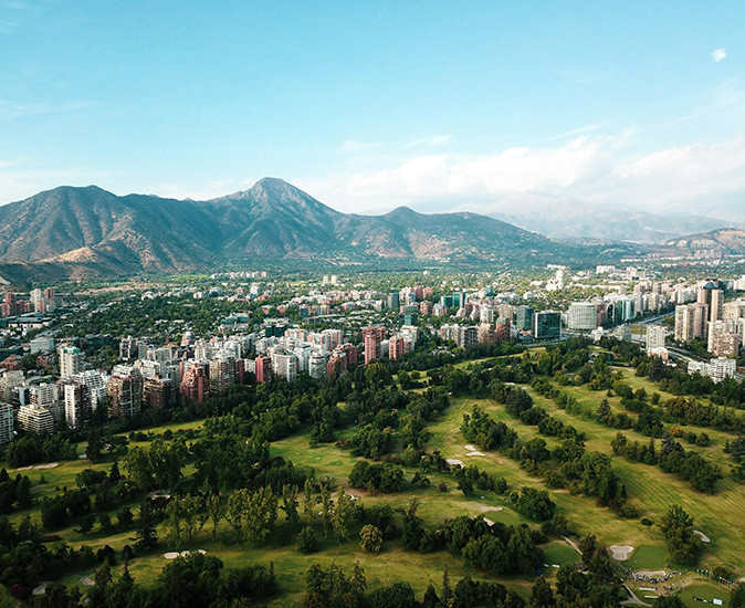 Moving to Santiago, Chile Aerial view of Santiago showing highrise buildings in a valley with a lot of green spaces and high mountains in the background