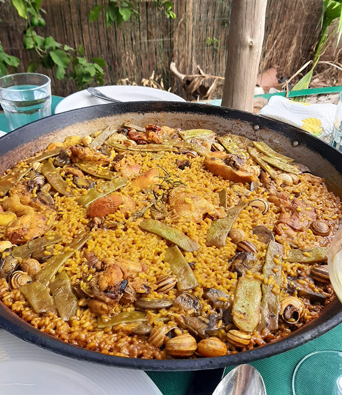 A paella at one of the best restaurants in Valencia A paella pan filled with traditional Valencian paella, set on a table surrounded by cutlery and water glasses