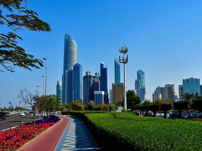 moving to Abu Dhabi aerial view of some of the highrise buildings in Abu Dhabi with a main road, sidewalk and some greenery in the foreground