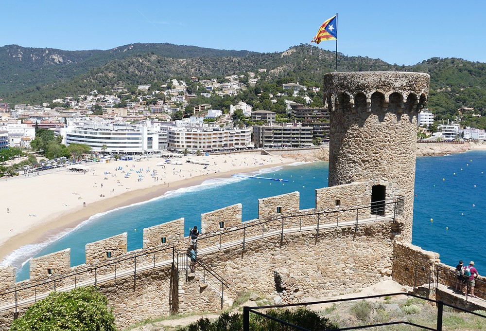 moving to Spain: things to know and where to live a castle in the foreground with a beach and high rise buildings in the background