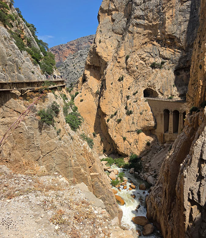 A valley with 2 cliffs, with a bridge on one side and a narrow walkway on the other