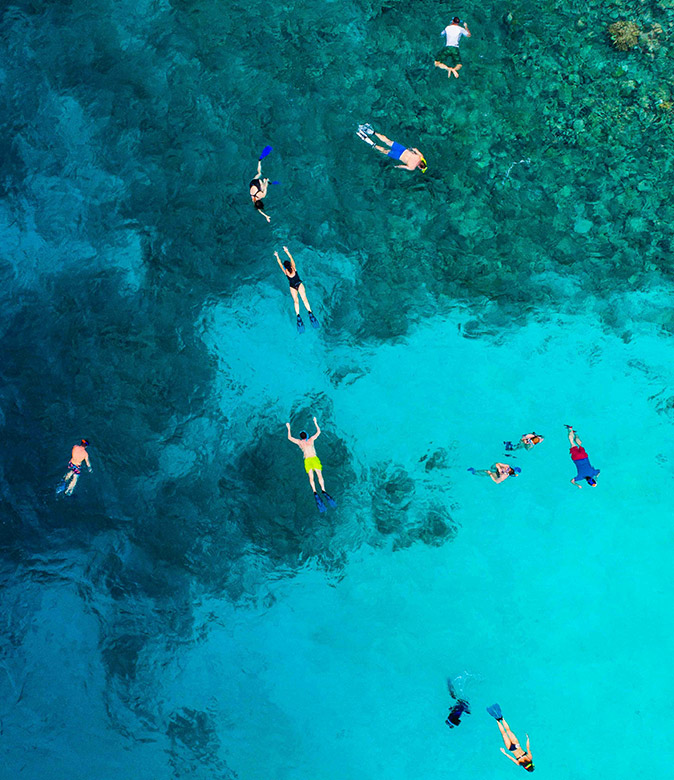 Snorkeling safety tips A group of snorkelers safely snorkeling above a reef in crystal clear water
