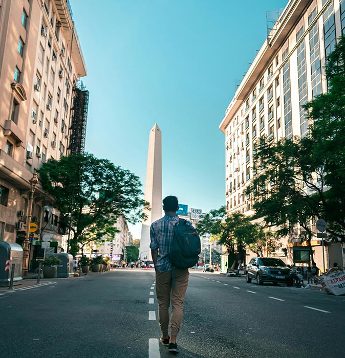 Living in Buenos Aires, Argentina as an expat a man walking in the middle of a road with highrise buildings on both sides and an obelisk in front of him
