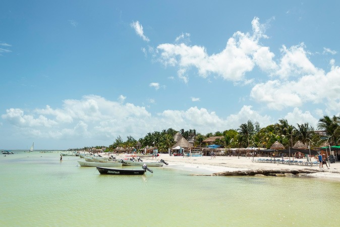 One of the best Caribbean islands for a laid-back vacaiton The coastline of a Caribbean island with several boats, a white sandy beach with beach bars and palm trees