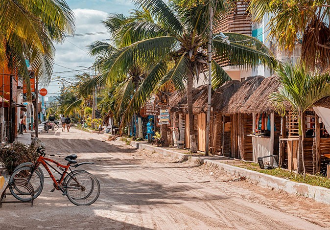 One of the best Caribbean islands to visit A sandy road with several small shops, palm trees and a few bicycles parked