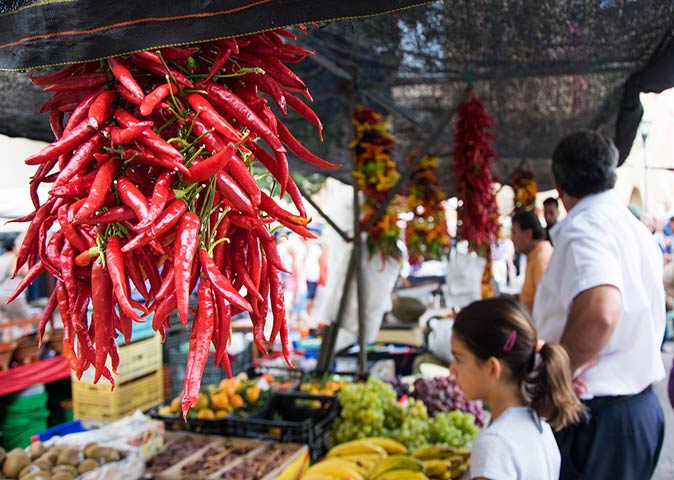 life in Spain a bunch of spicy peppers hanging in a market stall with a young girl and older man in the background