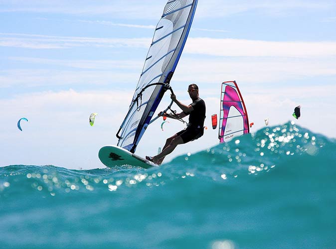 a guy windsurfing, a popular water sport in Miami a guy windsurfing in Miami, with kiteboarders in the background
