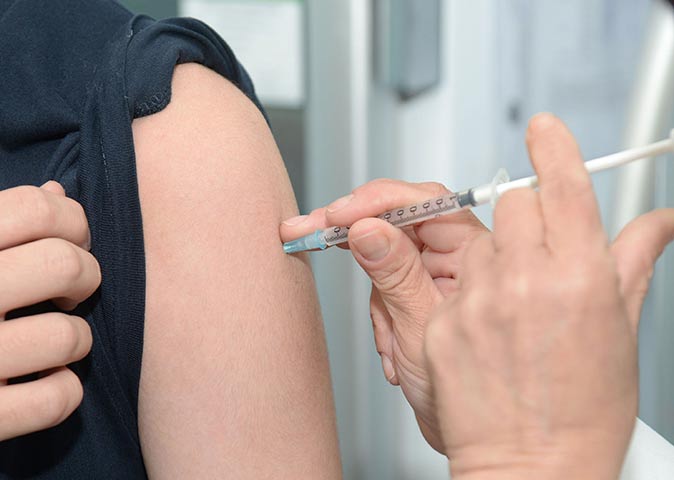 health insurance overseas two hands holding an needle placed on a person's upper arm