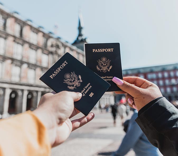 Moving to Spain as Americans two hands holding American passports, with the Plaza Mayor in Madrid in the backgroud