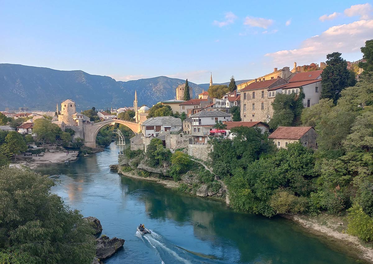 a small boat going down the river in Mostar with the old bridge in the background