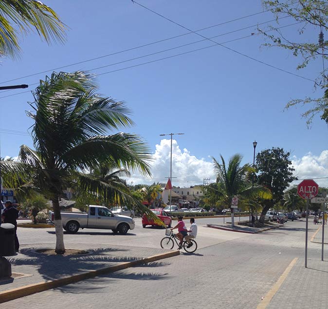 a bicycle and several cars on a main road in the center of Tulum
