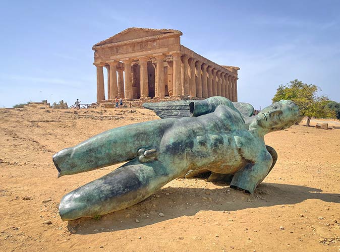 a broken statue of Icarus lying in the sand in front of of the Temple of Concordia in Valley of the Temples