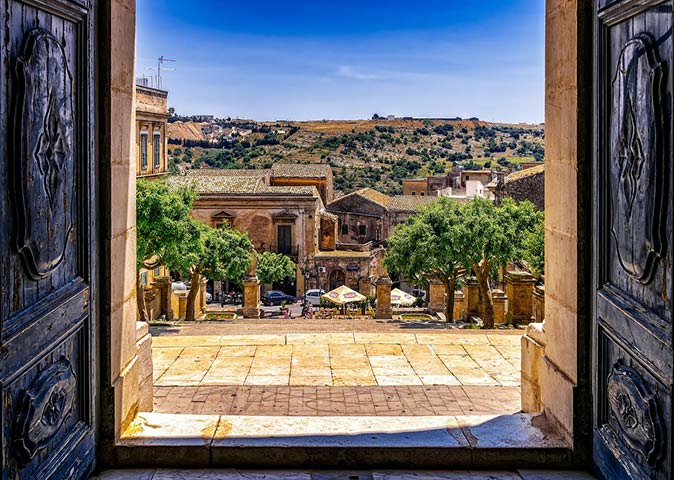 looking out through 2 large wooden doors over one of the most beautiful towns in Sicily, Modica