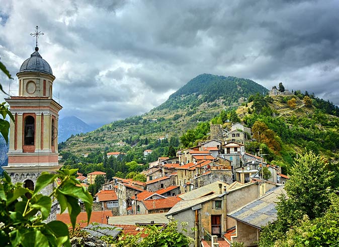 Triora is one of the best small towns in Italy to visit a church tower and the roofs of several houses set on a green hill in Italy