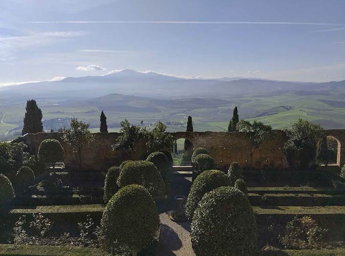 Pienza is a beautiful village in Italy to visit a landscaped garden in the foreground with a view of the roling hills in the green valley in the background