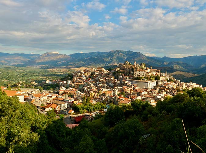 Castiglione di Sicilia is a beautiful village in Italy to visit an aerial view of a small Italian village surrounded by greenery and a cloudy sky
