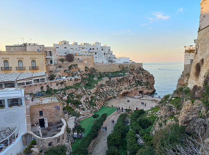 Polignano a Mare, a popular small town to visit in Italy a small rocky beach with several people, surrounded by houses on cliffs