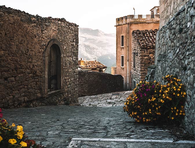 Montalbano Elicona is one of the most beautiful villages in Italy medieval stone buildings on a cobblestone road with yellow flowers on both sides