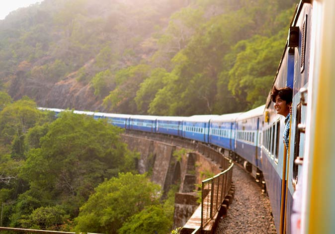 Working remotely and traveling in India a woman sticking her head out of a train in India in a green, mountainous setting