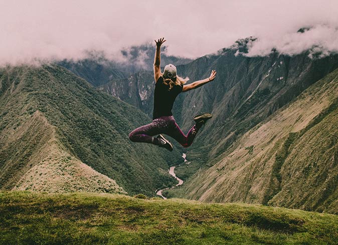Enjoying working remotely and traveling in Peru a woman facing away from the camera, jumping in the air with a green valley in the background