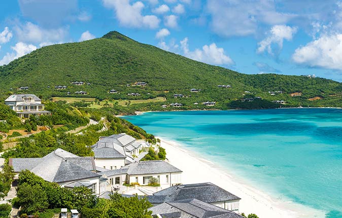 Mandarin Oriental, one of the most luxurious resorts in the Caribbean luxury villas set by a white sandy beach with green hills in the background and crystal clear water