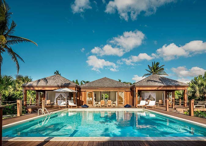 COMO Parrot Cay, one of the luxury hotels in the Caribbean worth staying at a swimming pool with behind that a large and luxurious villa with several sun loungers and palm trees
