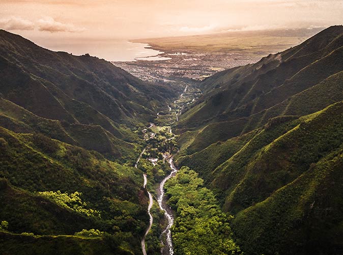 an aerial view of Maui showing green hills on both sides with a river in the middle and a city in the background