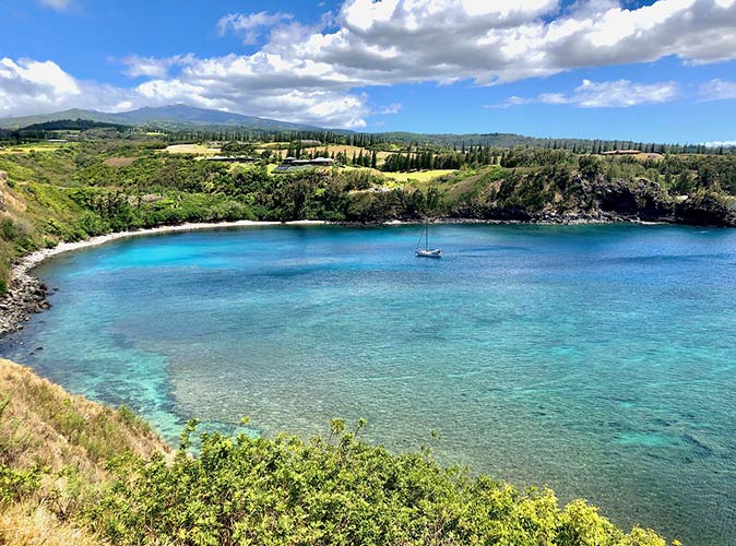 a bay with clear water and one sailboat, surrounded by green countryside