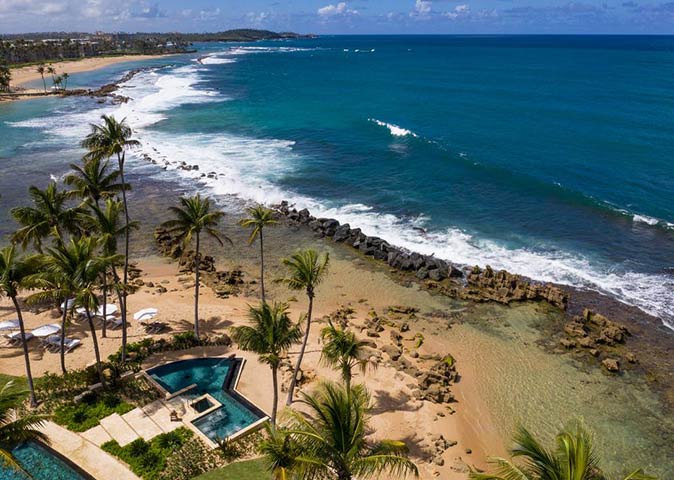 Dorado Beach, one of the most luxurious resorts in the Caribbean dark blue ocean, waves, a beach with rocks and part of a luxurious resort with palm trees.