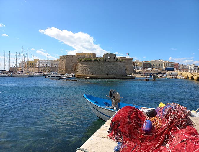 a red fishing net in the foreground with a medieval castle overlooking a marina in the background