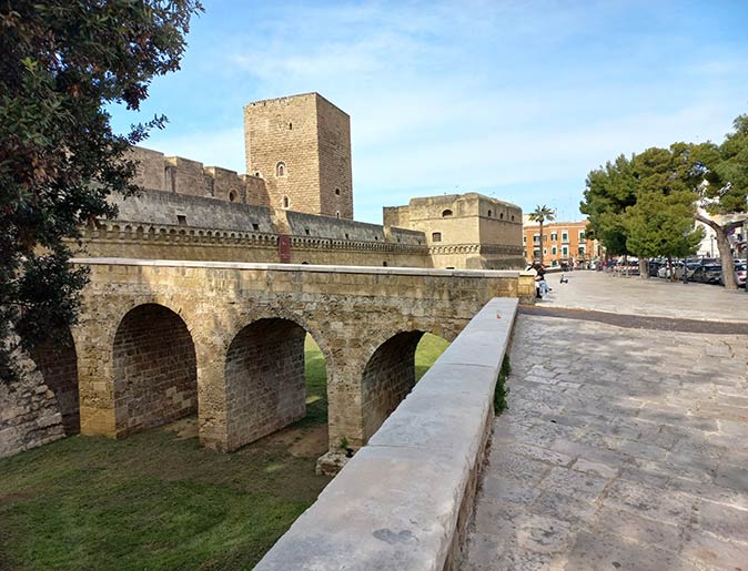 The Castello Svevo in Bari, Puglia a walkway next to a castle and an arched bridge