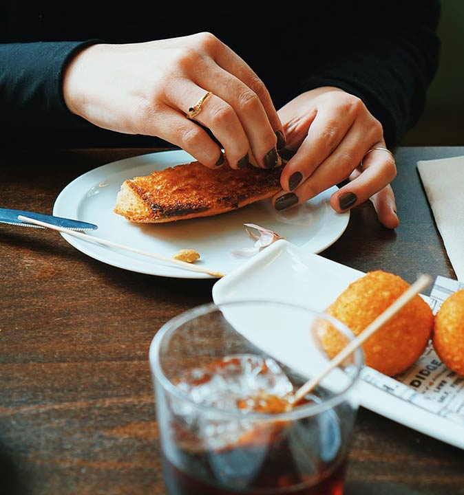 hands grabbing some bread with tapas and a glass of vermouth in the foreground
