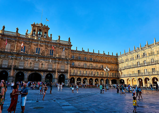 a large brown historic building surrounding a square with people