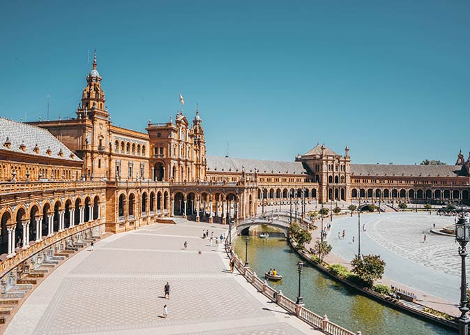 a brown arched building with a walkway and a river