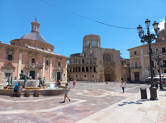 a city square with several people and a cathedral in the background