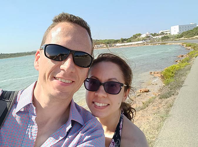 selfie of a man and a woman with a bit of coast and sea in the background and a blue sky